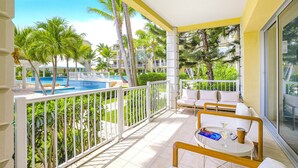 Ein Balkon mit Blick auf einen Swimmingpool, weißen Geländern und einer Sitzecke mit Tisch und Stühlen.