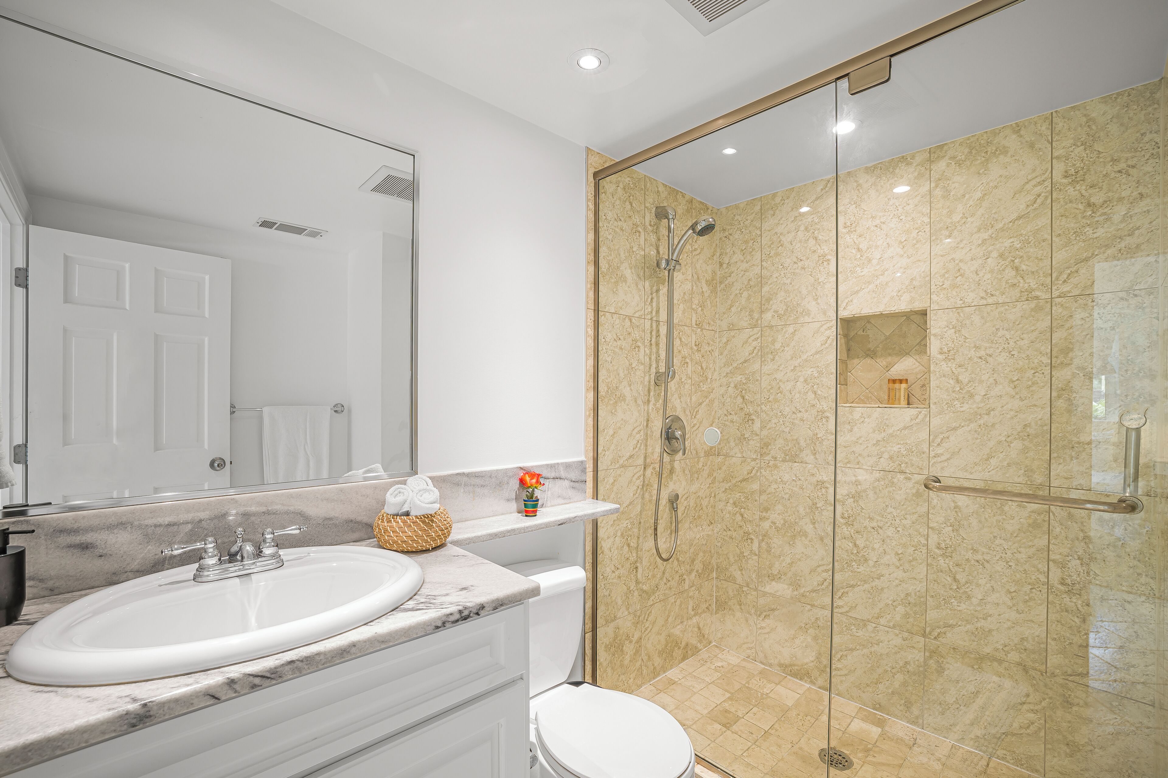 A bathroom with a white sink, a mirror, and a shower with beige tiles.