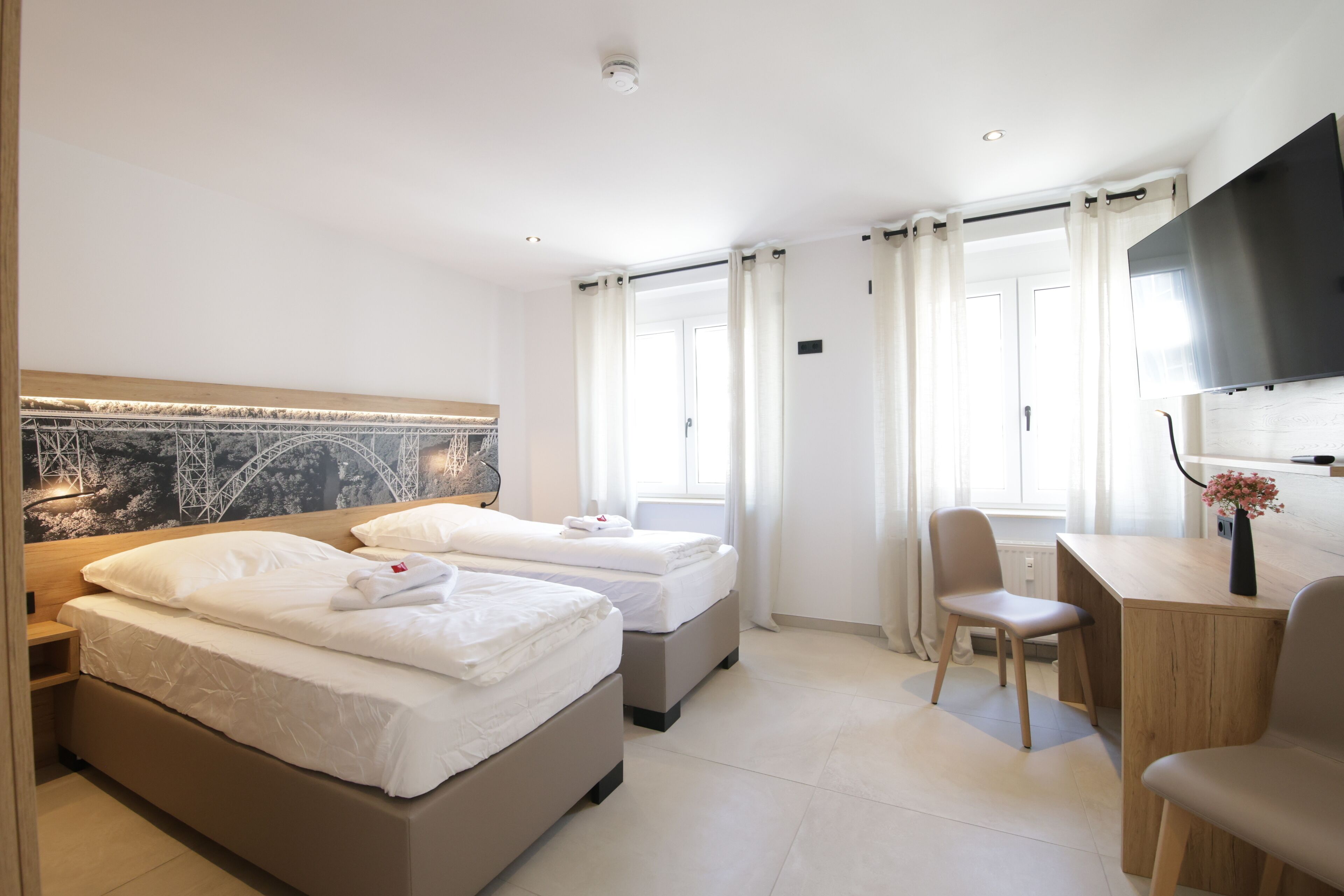 A hotel room with two beds, a desk, a chair, a TV, and a window with curtains.