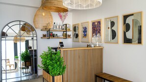 Zona de recepción con un mostrador de madera, un banco y un espejo grande. Hay estanterías con varios objetos y obras de arte enmarcadas en la pared.