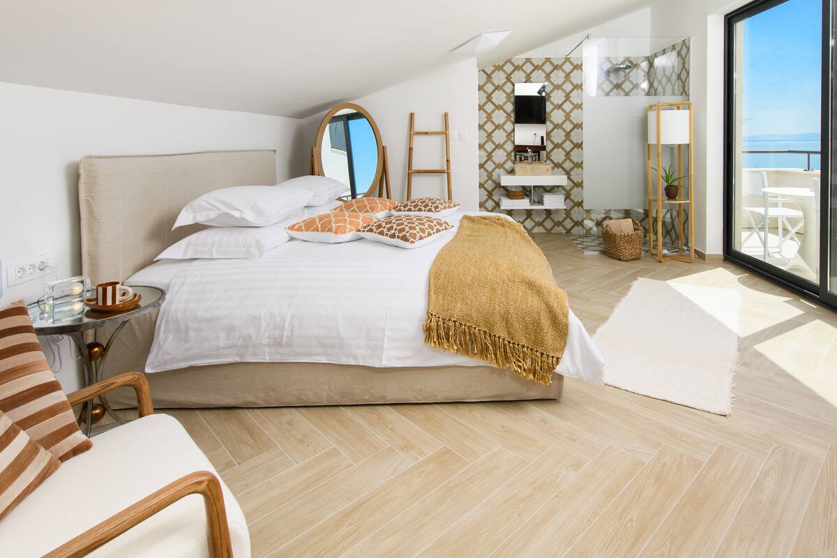 Un dormitorio moderno con una cama grande, una mesita de noche, una silla, un baño con ducha y un balcón con vistas.