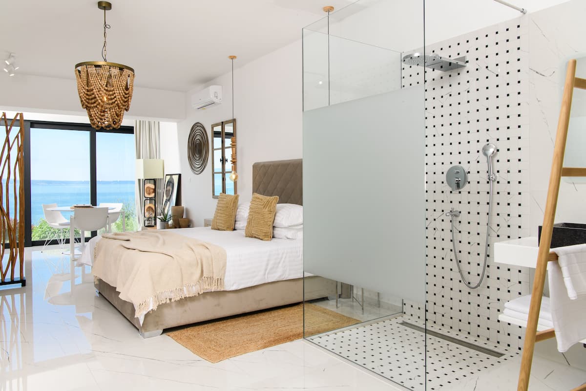 Un dormitorio moderno con una cama grande, cabina de ducha de vidrio y vista al mar.