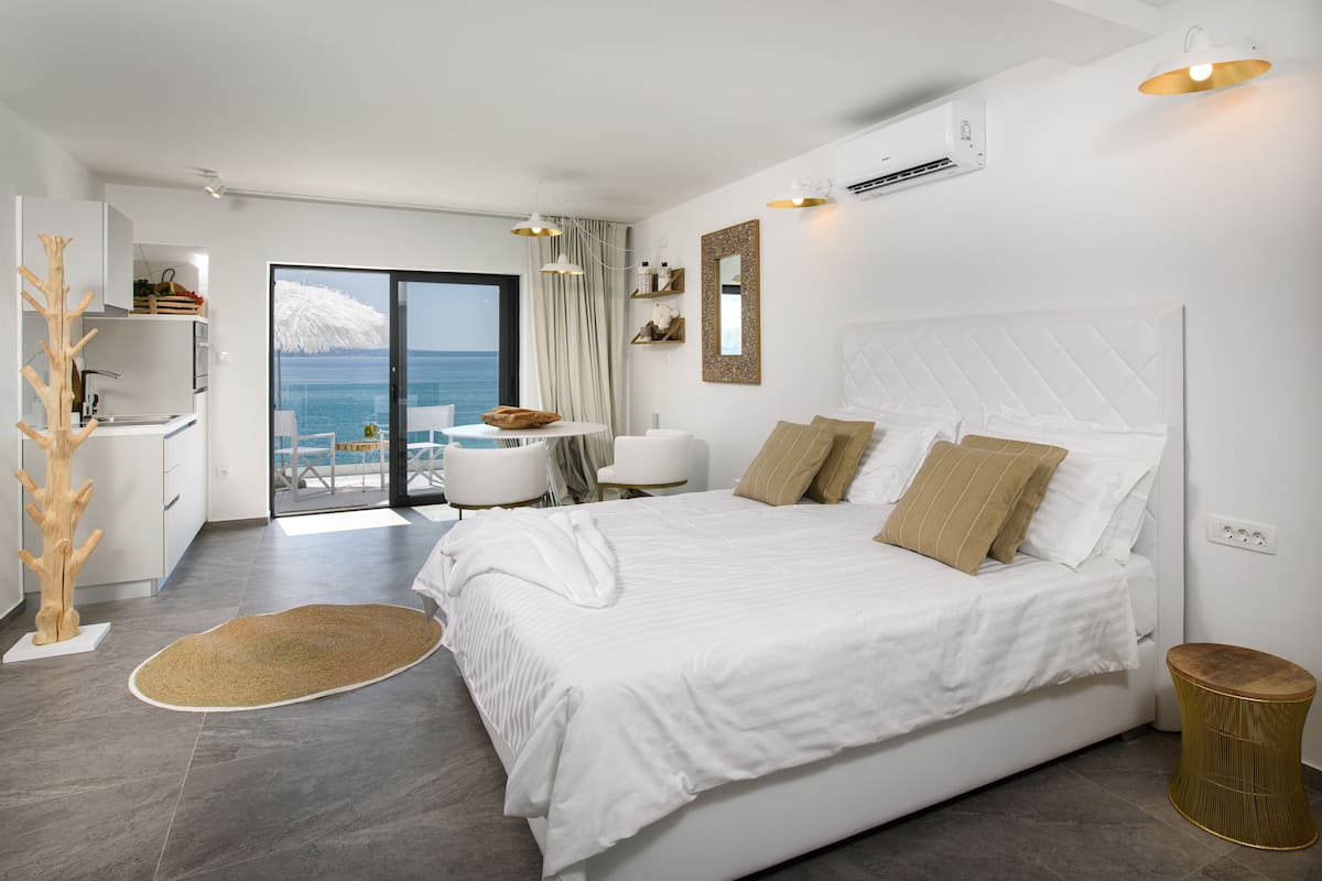 Un dormitorio moderno con una cama grande, vistas al mar, un balcón y una kitchenette.
