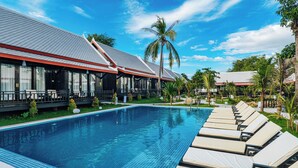 A swimming pool with lounge chairs, a covered area with tables and chairs, and palm trees.