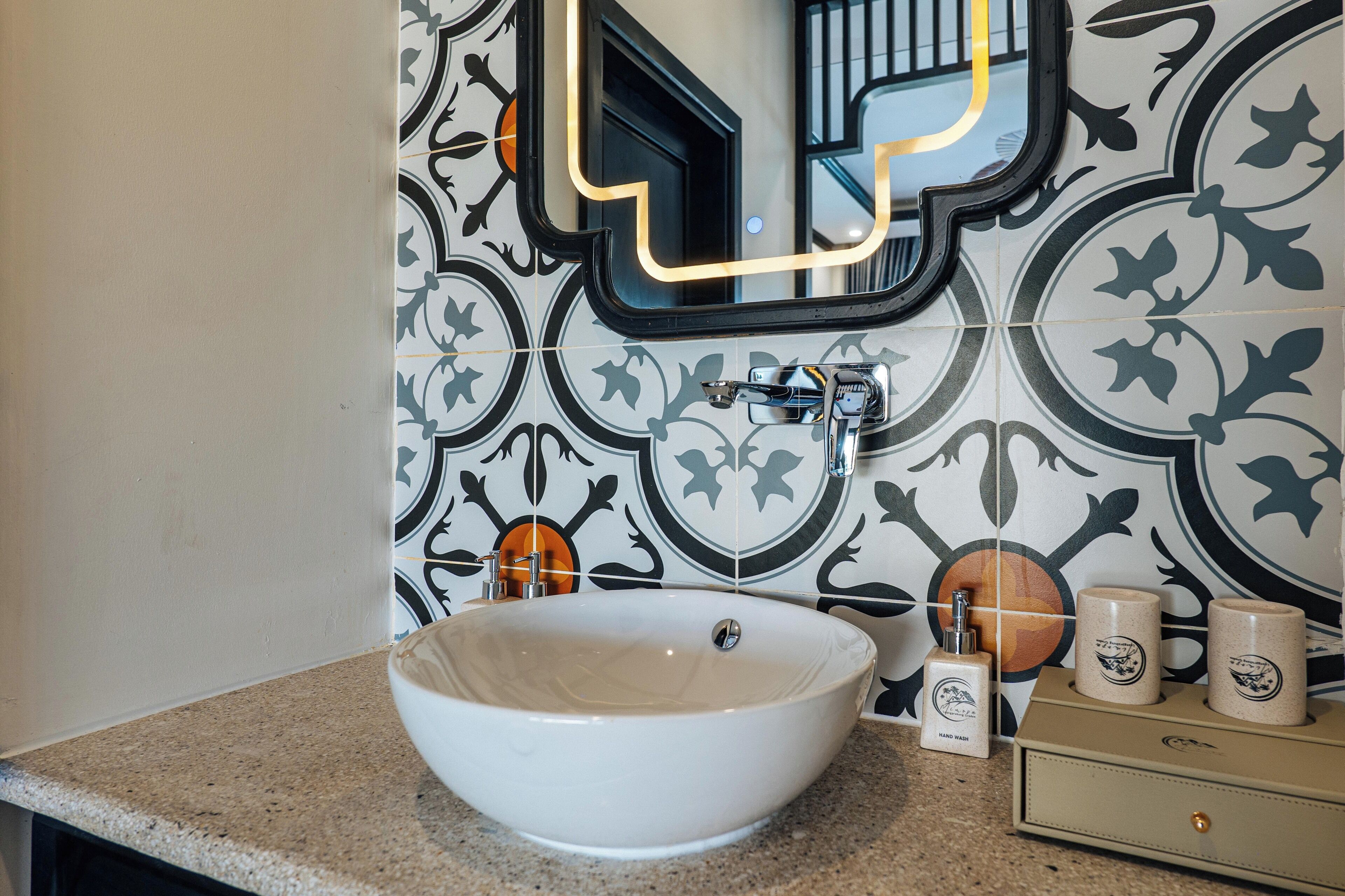 A bathroom with a large white vessel sink, a mirror, and a tiled wall with a geometric pattern.