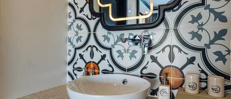 A bathroom with a large white vessel sink, a mirror, and a tiled wall with a geometric pattern.