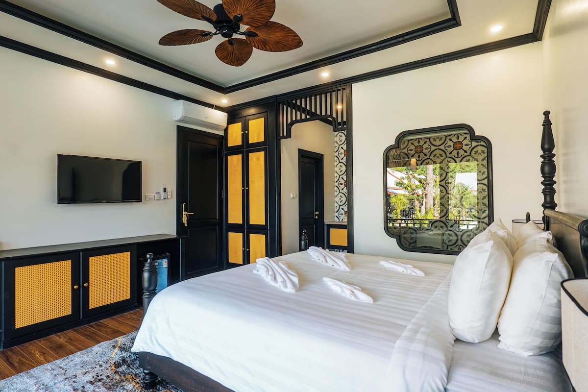 Un dormitorio con una cama grande, televisor, ventilador de techo y un espejo decorativo.