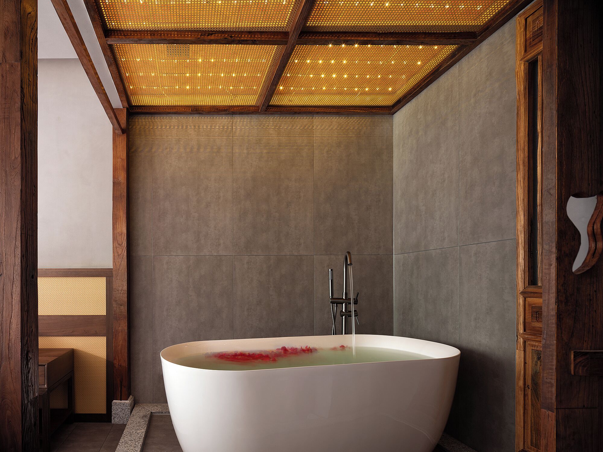 A modern bathroom with a freestanding bathtub, wooden beams, and a textured ceiling.