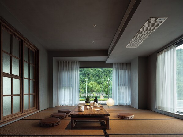 Una habitación japonesa tradicional con suelo de tatami, una mesa de madera baja y vistas a un bosque a través de amplios ventanales.