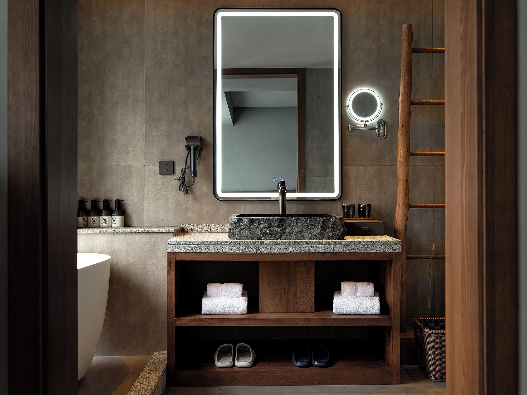 Une salle de bain moderne avec un grand miroir, un lavabo et une étagère où sont rangées des serviettes et des chaussures.