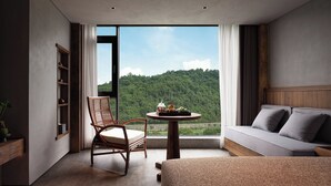 A modern room with a large window, a sofa, a chair, a table with a vase, and a wooden shelf. - Zhangjiajie SANHE Resort  (Zhangjiajie)