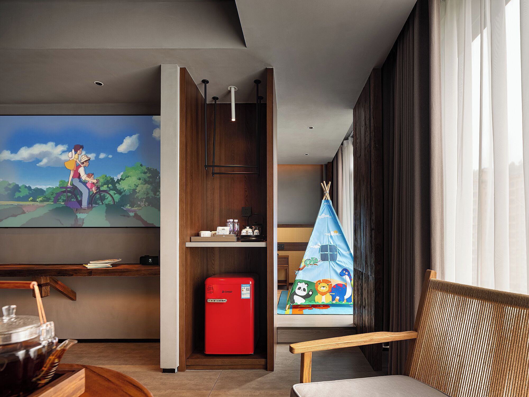 A modern living room with a flat-screen TV, a red Chigo refrigerator, a wooden cabinet, and a window with curtains.