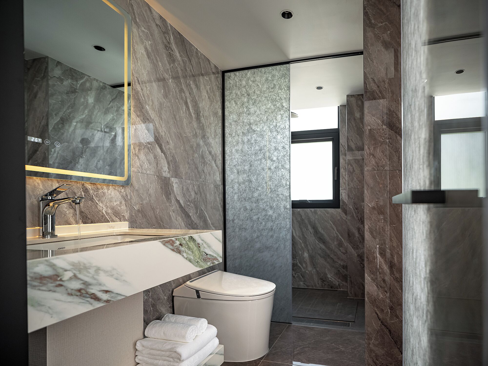 Een moderne badkamer met een marmeren wastafel, toilet en douche.