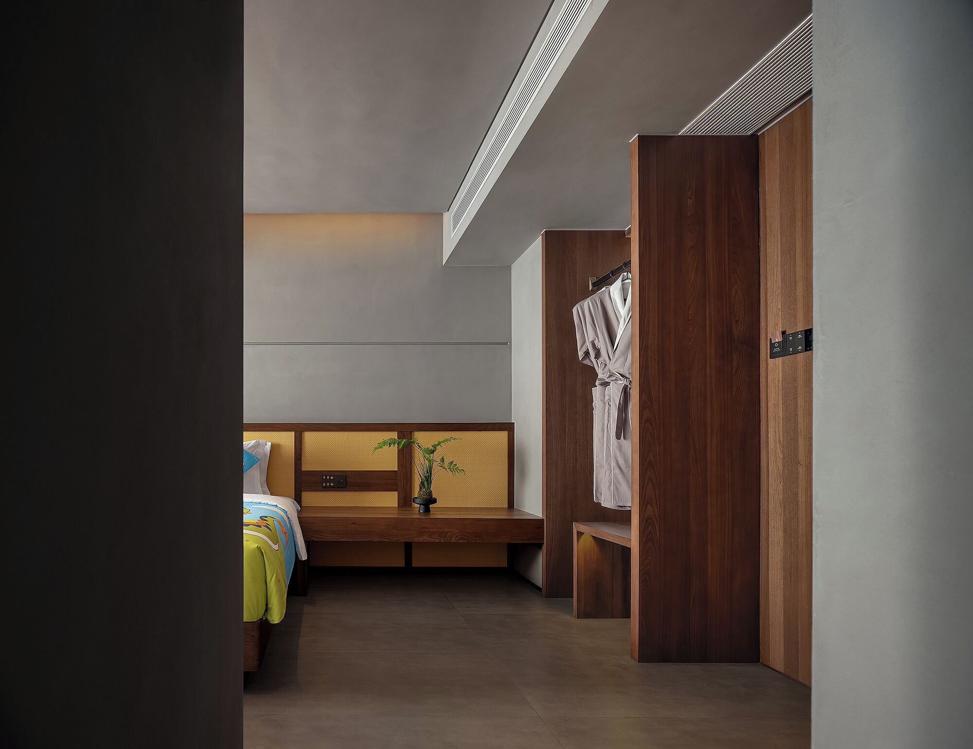 A modern hotel room with a wooden headboard, a bench, and a wardrobe.