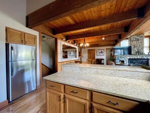 Una cocina con armarios de madera, encimera de granito, refrigerador de acero inoxidable, chimenea de piedra y techo de madera.