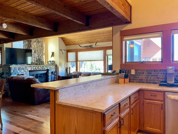 A spacious kitchen with wooden cabinets, a granite countertop, and a stone fireplace. - Big Sky Resort - Ski in and out Arrowhead Chalet 1657 (Big Sky)