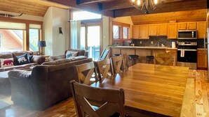 Amplia sala de estar con una mesa de comedor de madera, un conjunto de sofás y una cocina con armarios y electrodomésticos de madera.