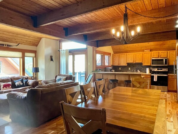 A spacious living area with a wooden dining table, a sofa set, and a kitchen with wooden cabinets and appliances. - Big Sky Resort - Ski in and out Arrowhead Chalet 1657 (Big Sky)