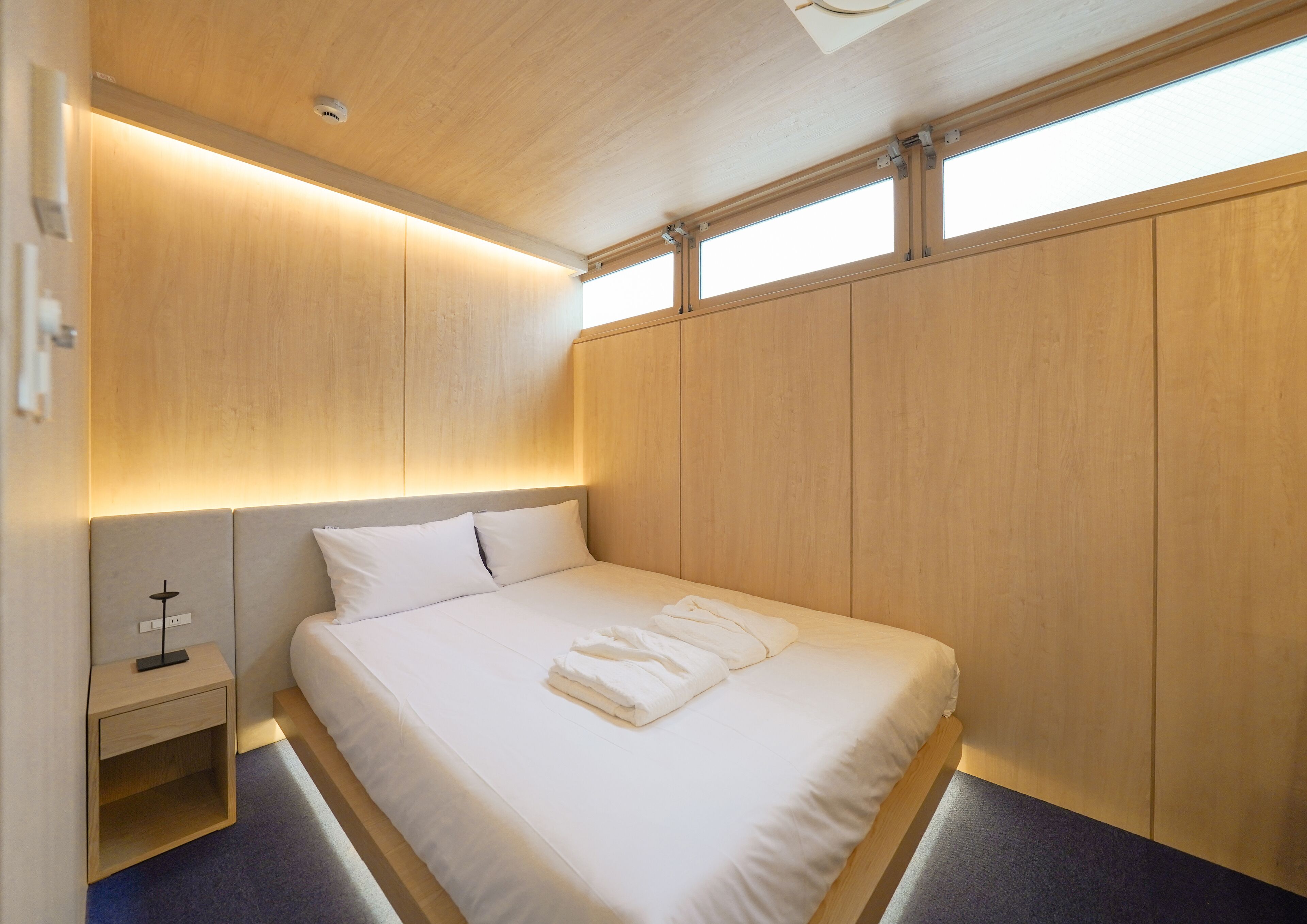 A modern bedroom with a wooden headboard, a bedside table, and a large window.