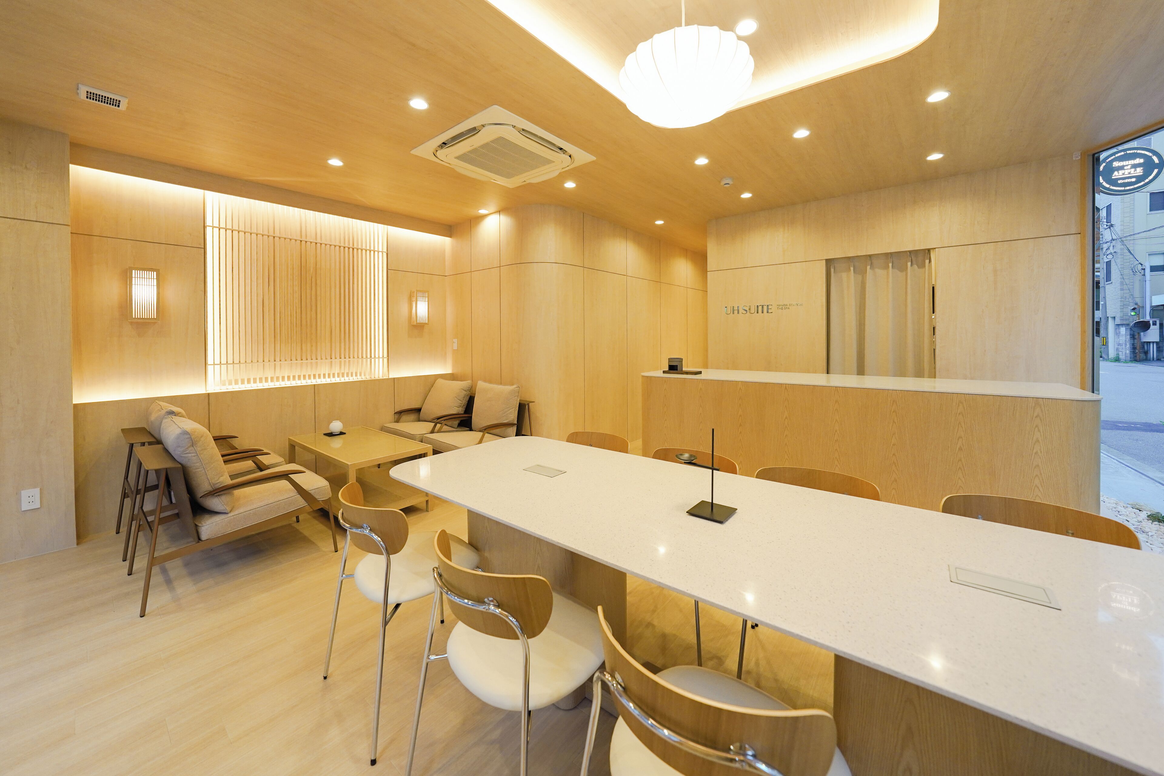A modern hotel lobby with a long reception desk, comfortable seating, and a large window offering a view of the street.