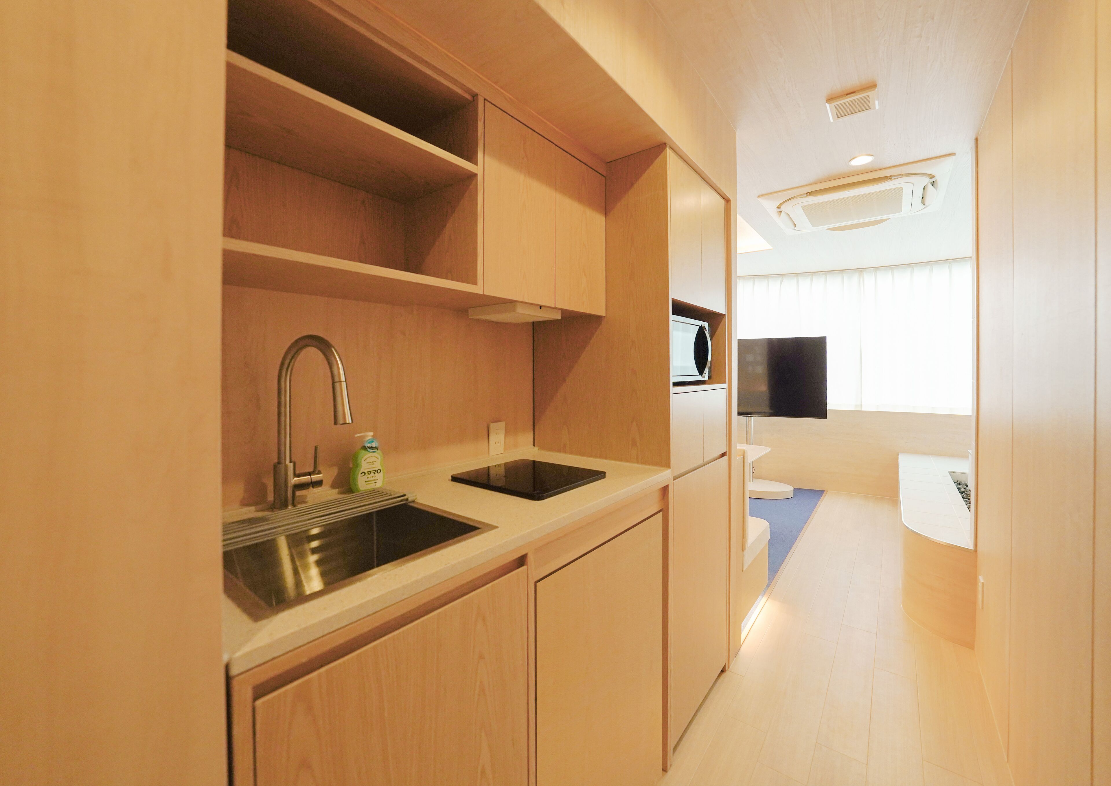 A compact kitchenette with a sink, microwave, and a flat-screen TV.