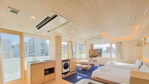 Quarto de hotel com cama, televisão, máquina de lavar, pequena kitchenette e janelas amplas.