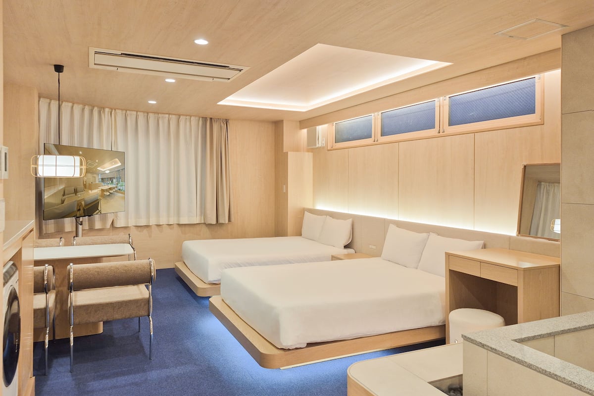 Una habitación de hotel moderna con dos camas, una zona de estar con sofá y sillones, un escritorio y un espejo grande.