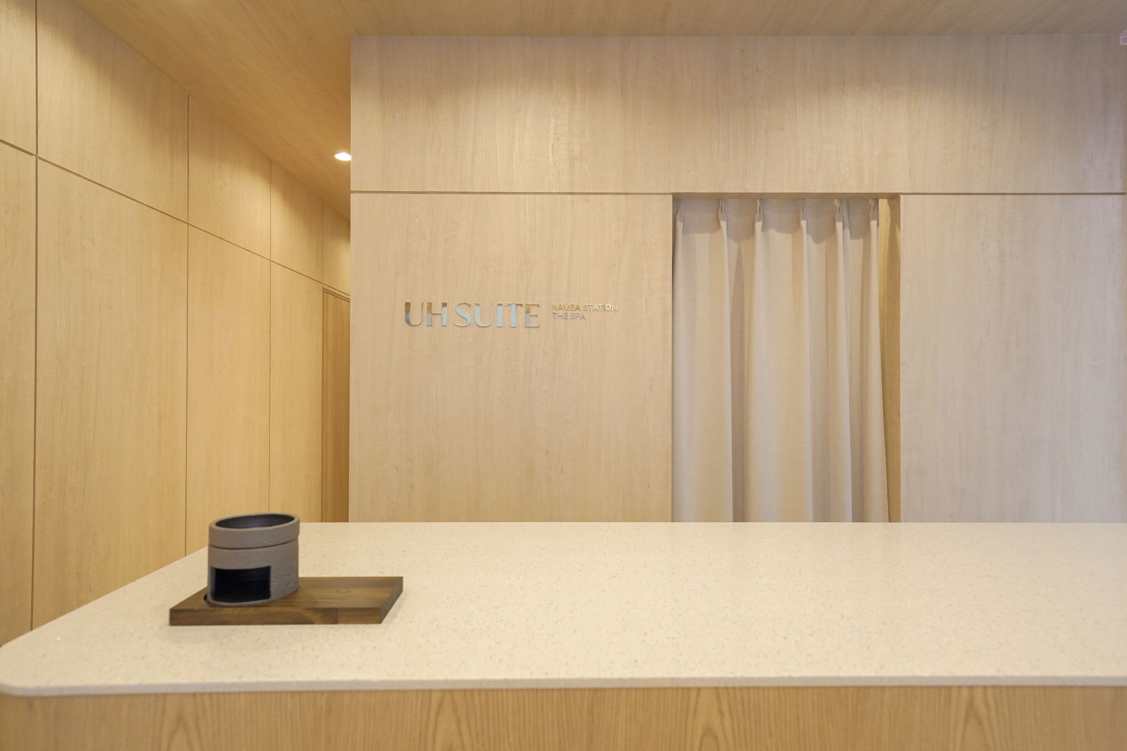 A reception area with a wooden panel wall, a reception desk, and a sign that reads 'UH SUITE NAVA STATION THESA SPA'.