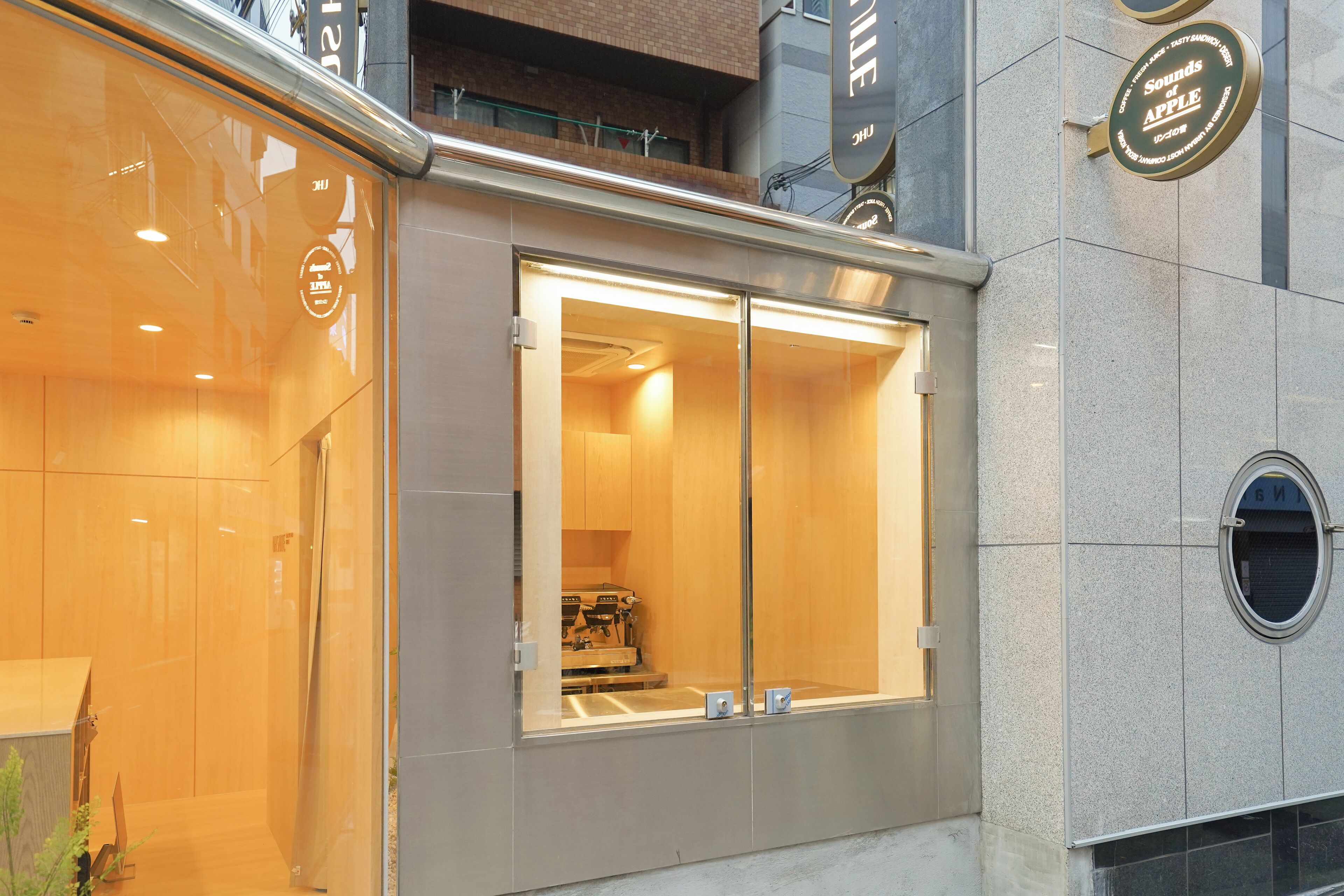 A modern building with a glass facade, a visible interior with a counter and equipment, and a sign indicating a restaurant or cafe.