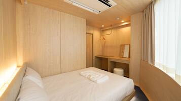Habitación de hotel con techo de madera, una cama con ropa de cama blanca, una mesita de noche pequeña, un espejo y una ventana con cortinas.