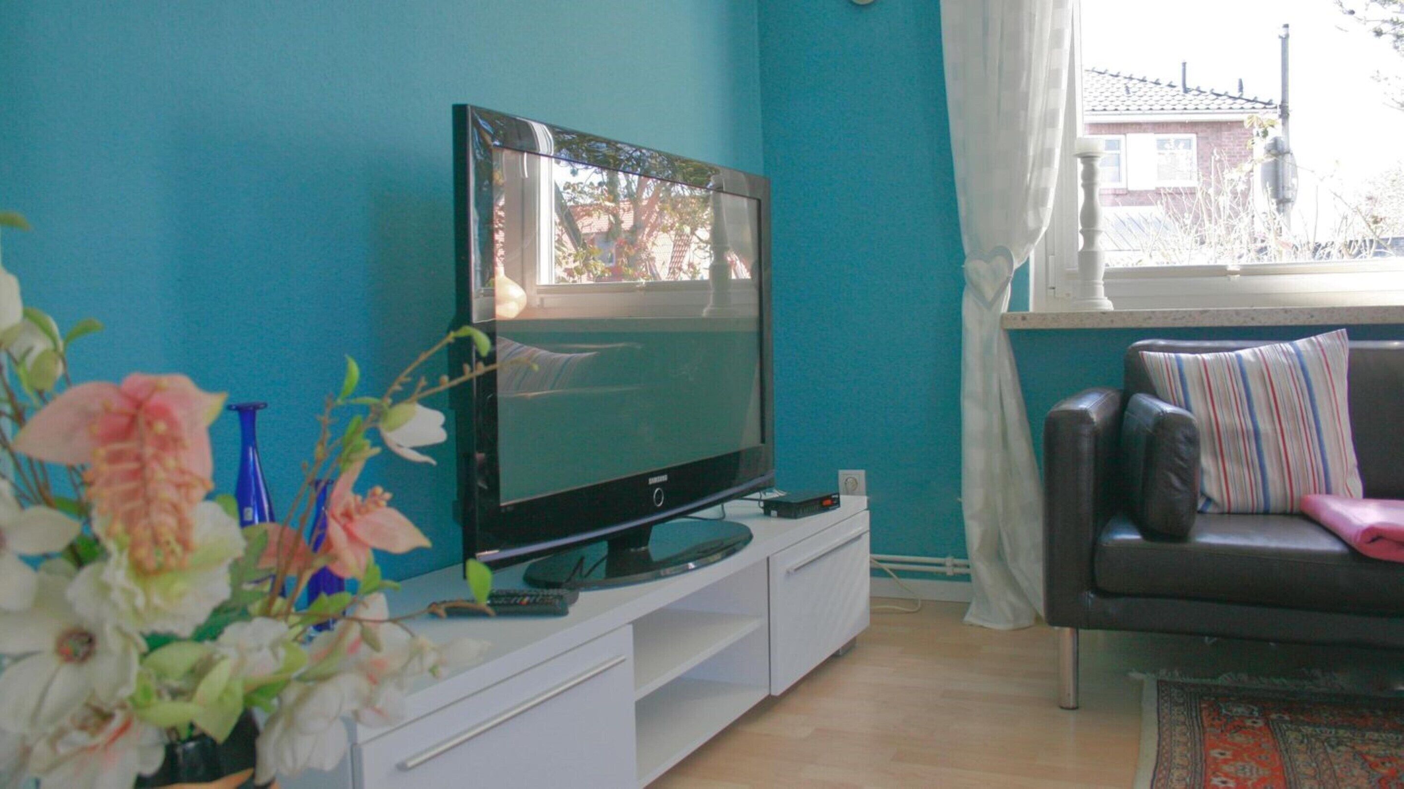 Un salon avec un téléviseur à écran plat posé sur un meuble de télévision blanc, un canapé marron agrémenté de coussins à rayures et une fenêtre ornée de rideaux légers.