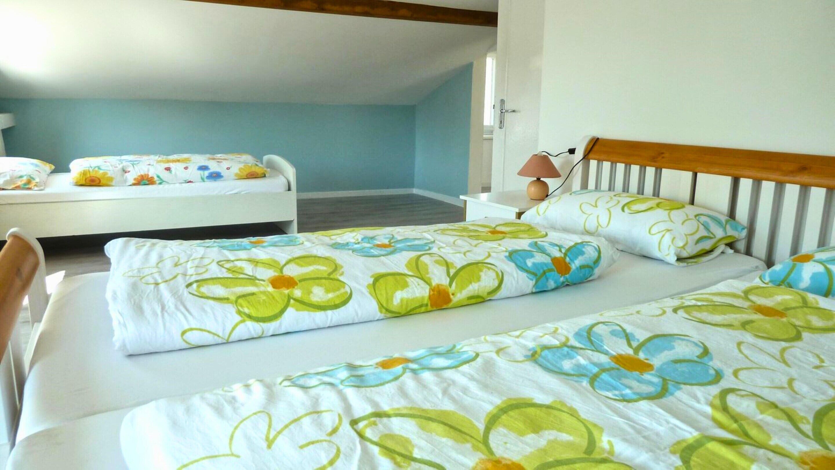 A bedroom with two beds, a nightstand, a lamp, and a door leading to another room.