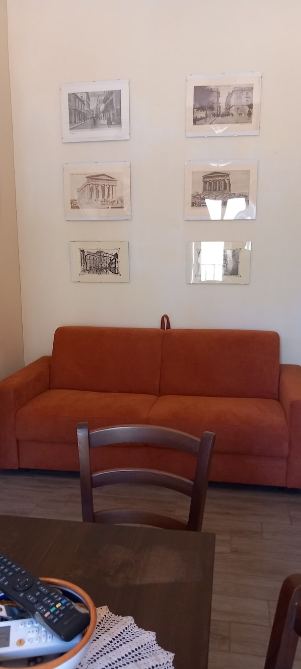 Un saló amb un sofà vermell, una cadira de fusta i una taula amb un comandament a distància.
