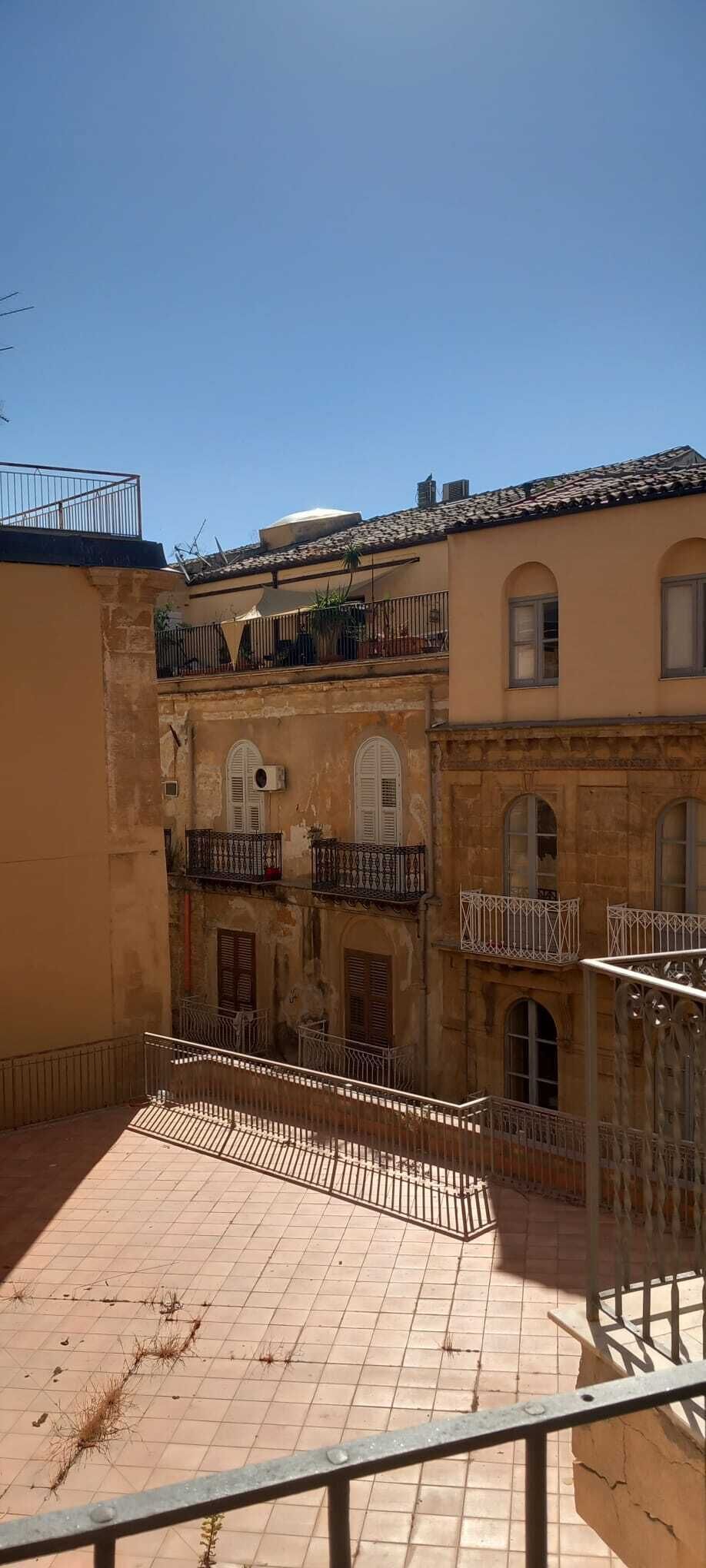 Une cour avec un sol carrelé, un bâtiment doté d’un balcon et d’une balustrade.