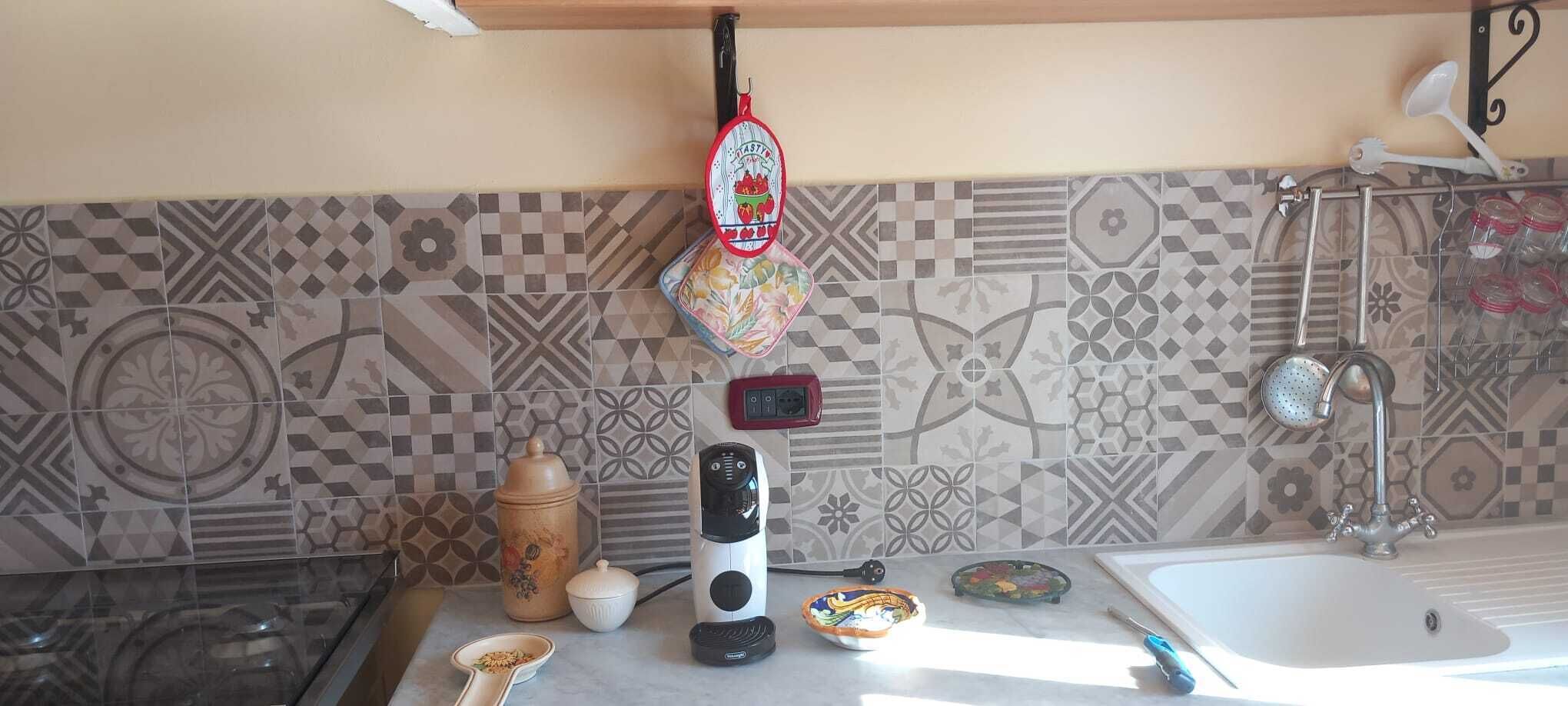 Une cuisine avec des carreaux décoratifs, une bouilloire, une machine à café, un grille-pain et un évier.