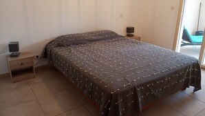 A bedroom with a bed, a bedside table with a speaker, and a chair in the corner.