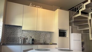 Une cuisine moderne avec des meubles blancs, un pare-feu décoré, un micro-ondes encastré, un réfrigérateur blanc et une table de salle à manger ronde dotée d’un îlot central.