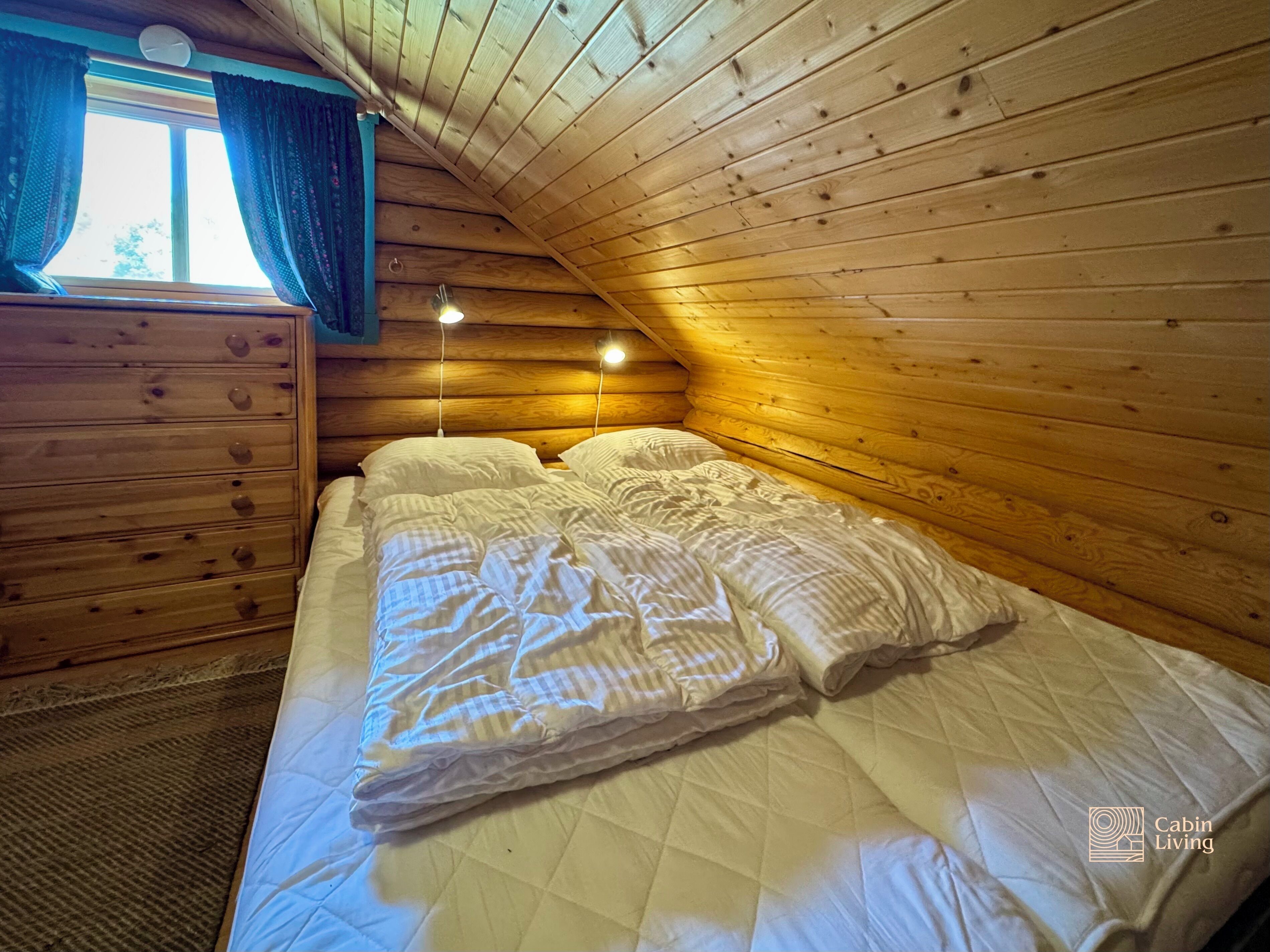 Une chambre confortable dans un chalet, avec un plafond en bois, un lit recouvert de draps blancs, une commode et une fenêtre avec des rideaux.