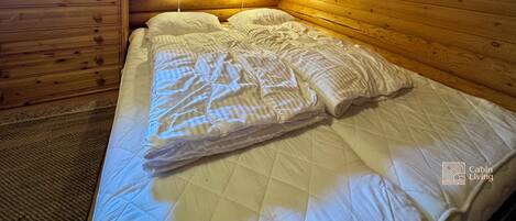 Une chambre confortable dans un chalet, avec un plafond en bois, un lit recouvert de draps blancs, une commode et une fenêtre avec des rideaux.