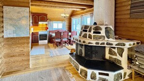 L’intérieur d’une cabane comprend une cheminée en pierre, une table à manger en bois et un coin cuisine avec un poêle.