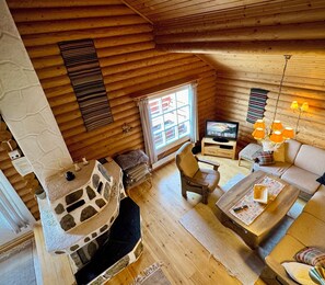 A cozy cabin interior with a stone fireplace, wooden furniture, and a television.