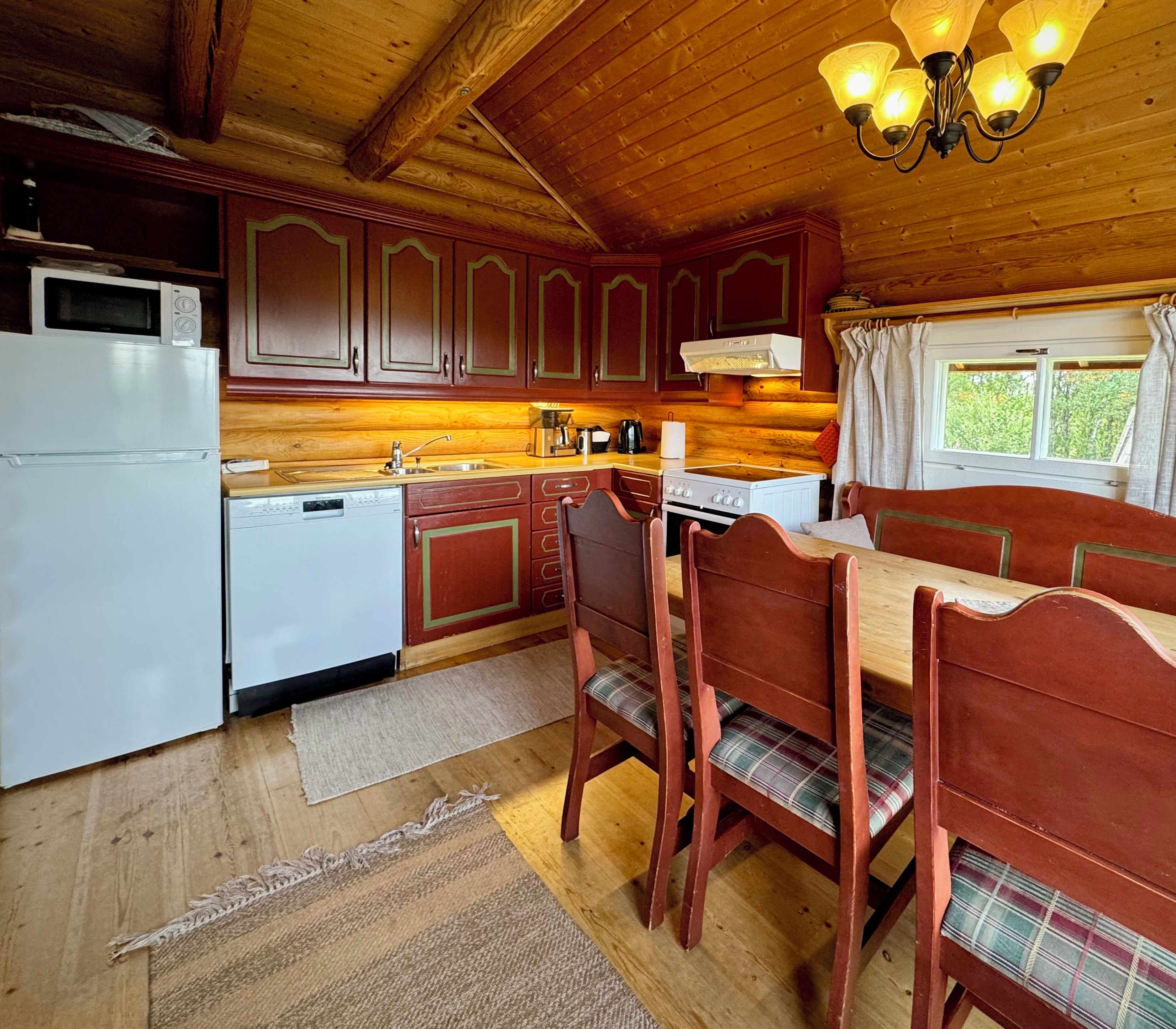Een keuken in blokhutstijl met houten kastjes, een eettafel met stoelen, een koelkast en een fornuis.