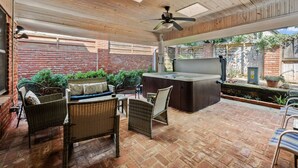 Eine Terrasse im Freien mit Korbmöbeln, einem Whirlpool und einer Backsteinwand als Hintergrund.