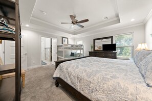 A bedroom with a bunk bed, a ceiling fan, a dresser, a TV, and a window with blinds.