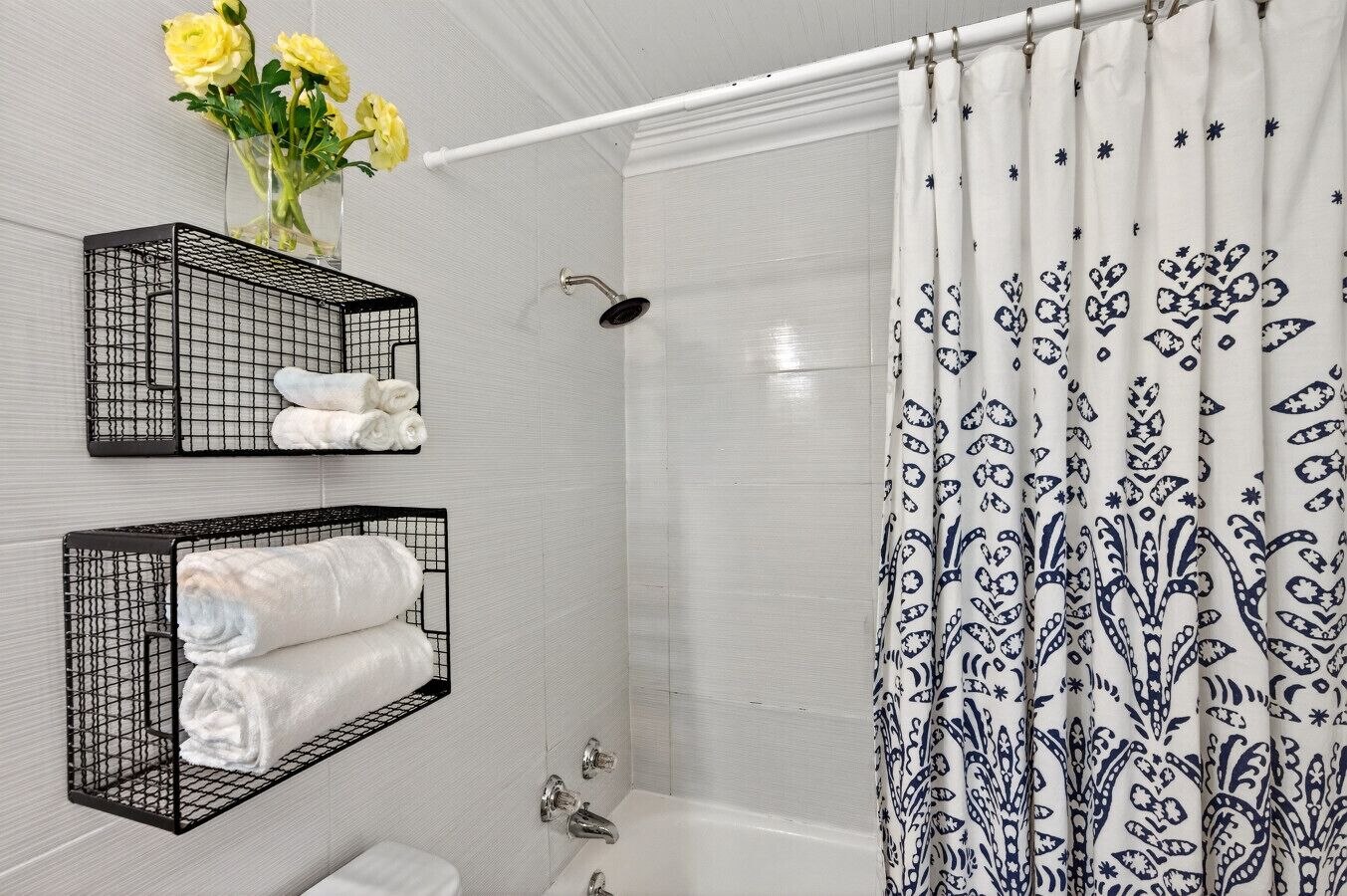 A bathroom with a shower, two towel racks with towels, a toilet, and a shower curtain with a floral pattern.