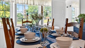 A dining table set with plates, bowls, and glasses, surrounded by wooden chairs.