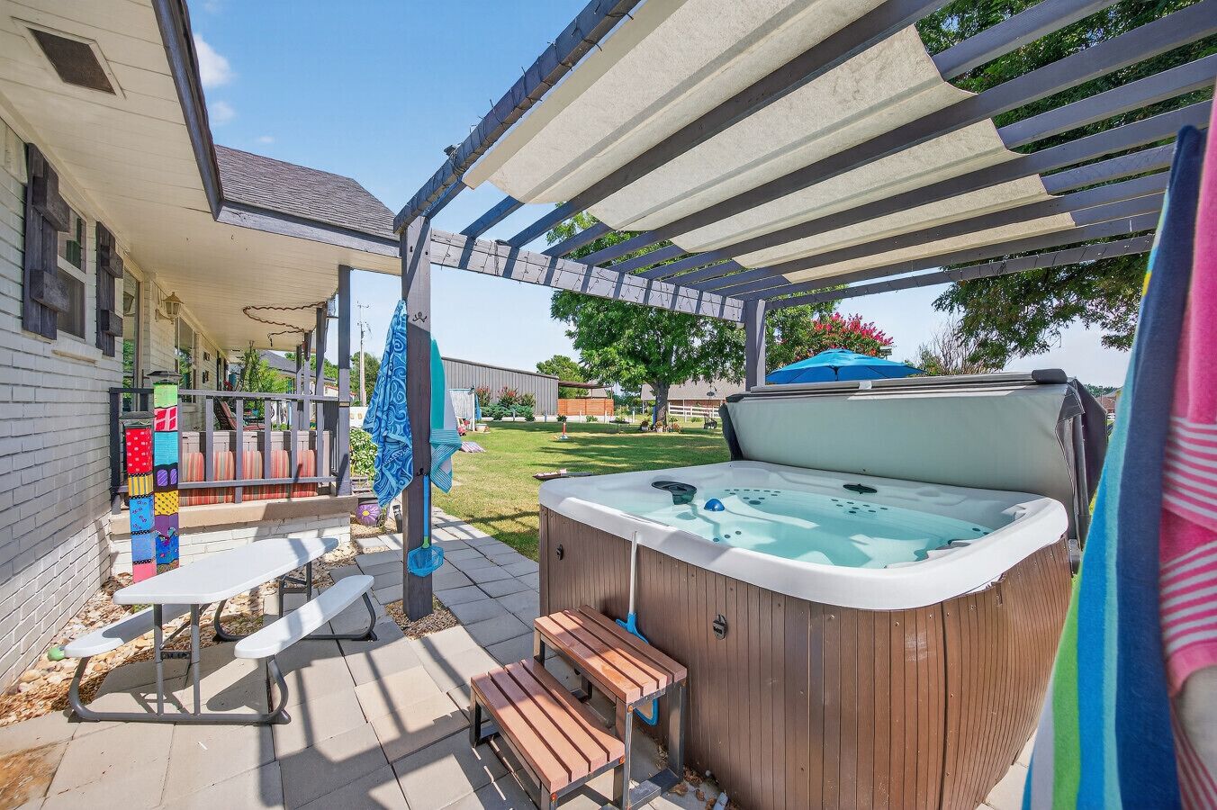 A backyard with a hot tub, wooden benches, a pergola, and a colorful play structure.