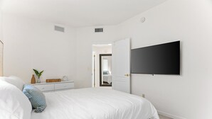 A bedroom with a bed, a dresser, a TV mounted on the wall, and a door leading to another room. - Close to downtown, U of A, I-10, hospitals and extraordinary hiking and biking! (Tucson)