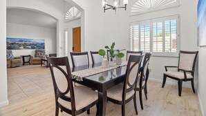 A dining area with a dark wooden table, six chairs, a chandelier, and a large window with blinds. - Close to downtown, U of A, I-10, hospitals and extraordinary hiking and biking! (Tucson)