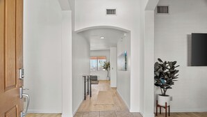 A hallway with a wooden door, a small table with a chair, a potted plant, and a painting on the wall. - Close to downtown, U of A, I-10, hospitals and extraordinary hiking and biking! (Tucson)
